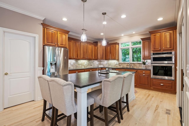 kitchen with a center island, stainless steel appliances, light hardwood / wood-style flooring, crown molding, and pendant lighting