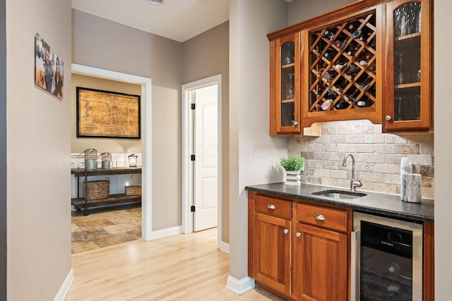 bar featuring sink, light hardwood / wood-style flooring, decorative backsplash, dark stone countertops, and beverage cooler