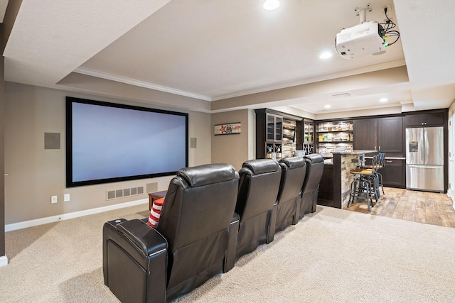 home theater featuring a raised ceiling, light colored carpet, crown molding, and bar