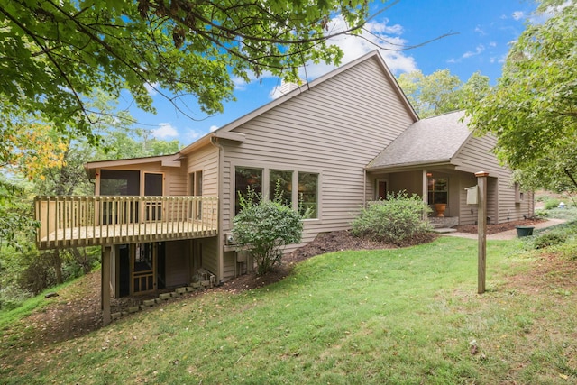 rear view of property featuring a lawn, a sunroom, and a deck