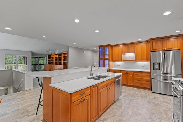 kitchen with sink, a kitchen breakfast bar, backsplash, a center island with sink, and appliances with stainless steel finishes