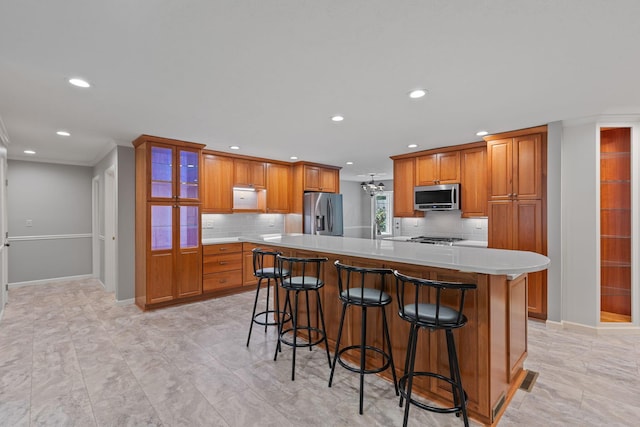 kitchen featuring a large island, stainless steel appliances, a kitchen breakfast bar, backsplash, and ornamental molding