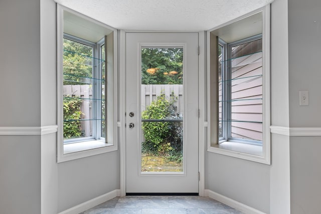 entryway with a healthy amount of sunlight, light tile patterned floors, and a textured ceiling