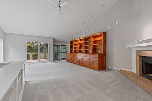 unfurnished living room featuring track lighting, a textured ceiling, light colored carpet, ceiling fan, and a fireplace