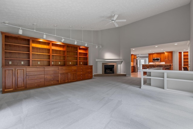 unfurnished living room with a high ceiling, a textured ceiling, light colored carpet, and ceiling fan