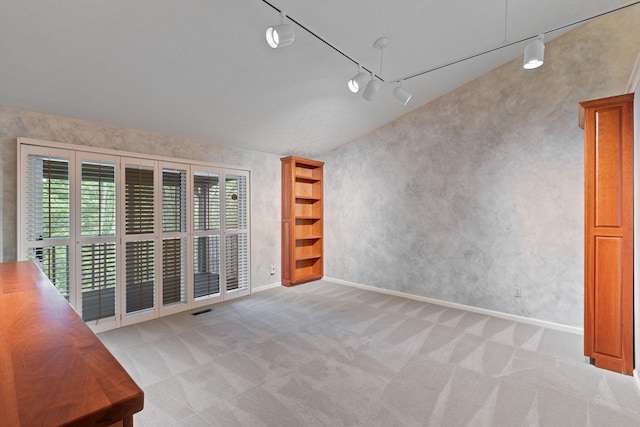 carpeted empty room with track lighting and lofted ceiling