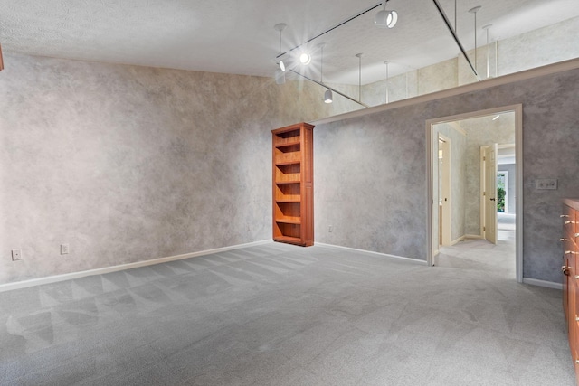 carpeted empty room featuring a towering ceiling, a textured ceiling, and track lighting