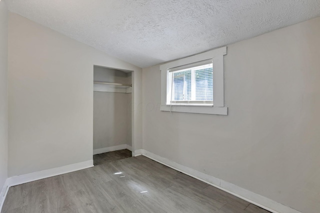 unfurnished bedroom with vaulted ceiling, a closet, wood-type flooring, and a textured ceiling