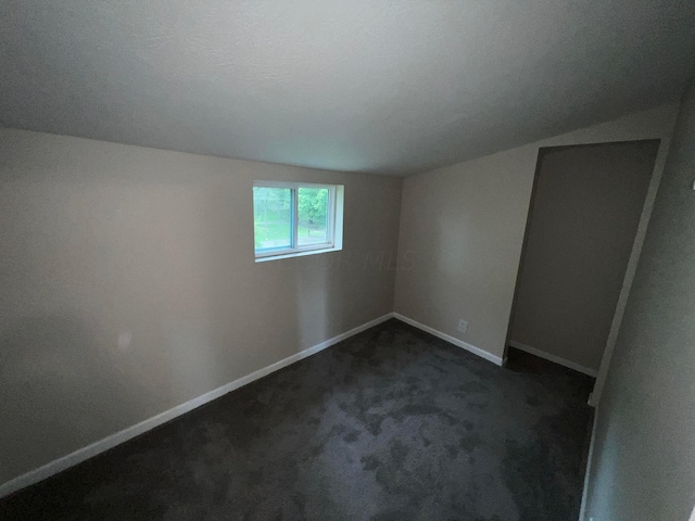 spare room featuring dark colored carpet and lofted ceiling