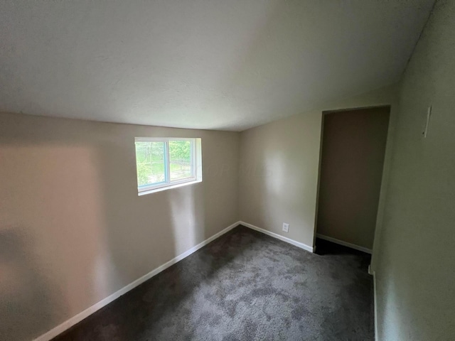 spare room with dark colored carpet and lofted ceiling