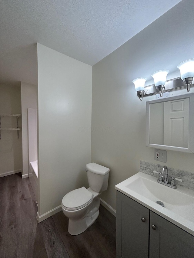 bathroom featuring a bath, a textured ceiling, toilet, vanity, and hardwood / wood-style flooring