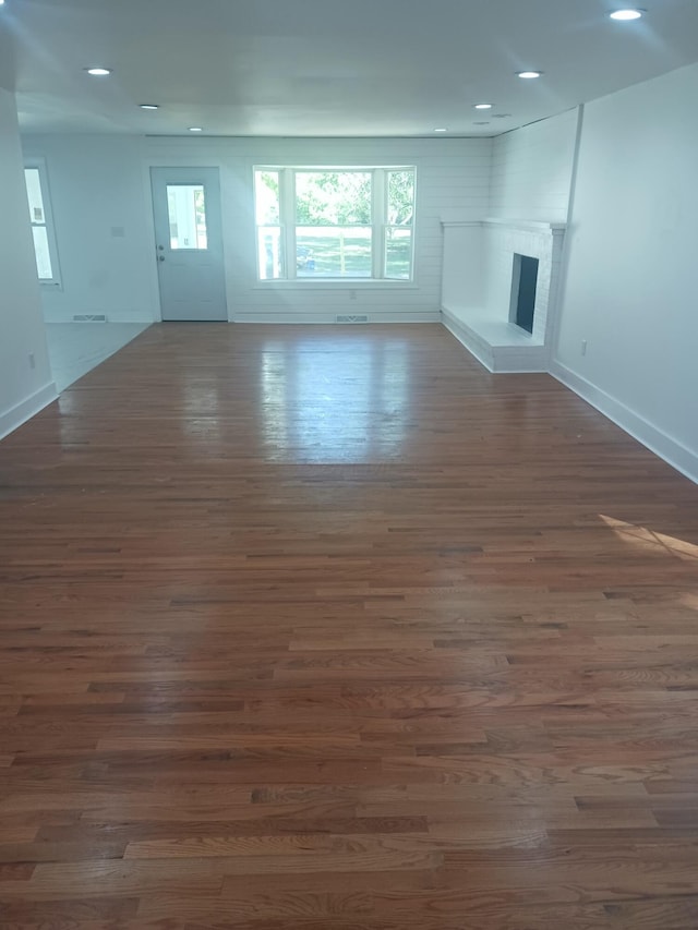 unfurnished living room with a brick fireplace and dark wood-type flooring