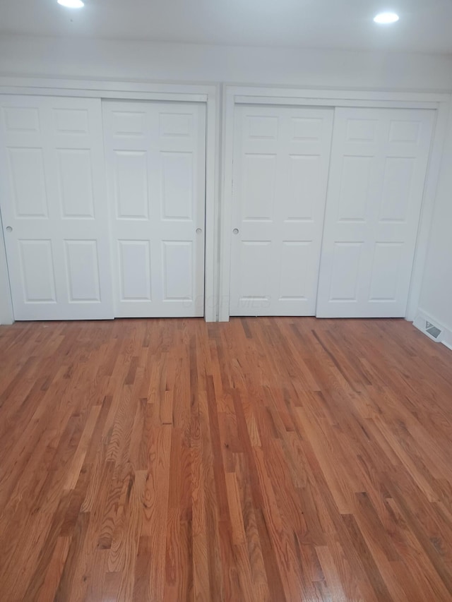 unfurnished bedroom with wood-type flooring and multiple closets