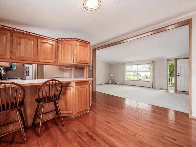 kitchen featuring a kitchen bar, kitchen peninsula, dark hardwood / wood-style flooring, ornamental molding, and a textured ceiling