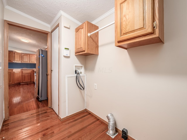 clothes washing area with cabinets, hookup for a washing machine, a textured ceiling, crown molding, and hardwood / wood-style flooring