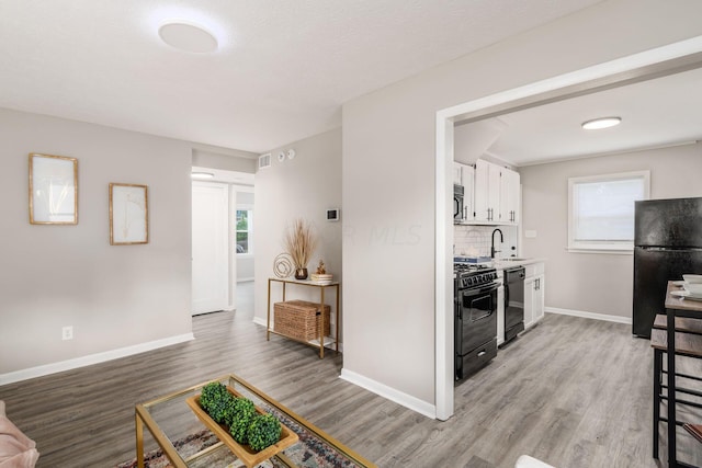 kitchen featuring sink, backsplash, light hardwood / wood-style floors, white cabinets, and black appliances