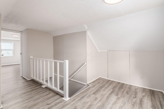 bonus room featuring light hardwood / wood-style floors, lofted ceiling, and a textured ceiling