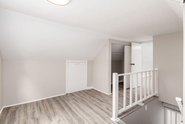 bonus room with a textured ceiling, light wood-type flooring, and vaulted ceiling