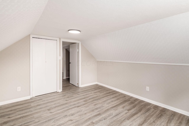 additional living space with a textured ceiling, light hardwood / wood-style floors, and vaulted ceiling