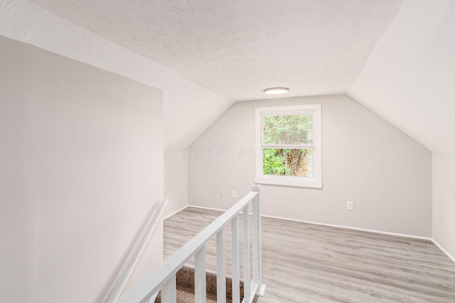 additional living space featuring a textured ceiling, light wood-type flooring, and lofted ceiling