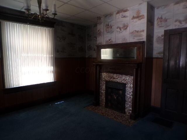 unfurnished living room featuring dark colored carpet, a paneled ceiling, an inviting chandelier, and a tiled fireplace