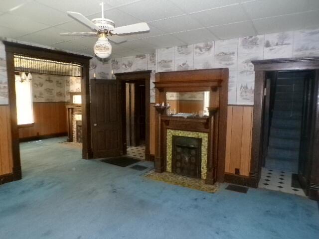 unfurnished living room featuring ceiling fan, wood walls, carpet floors, and a tiled fireplace