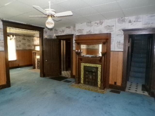 2343 Indianola Ave, Columbus, OH 43202 - unfurnished living room featuring wainscoting, a fireplace with flush hearth, wallpapered walls, a paneled ceiling, and ceiling fan
