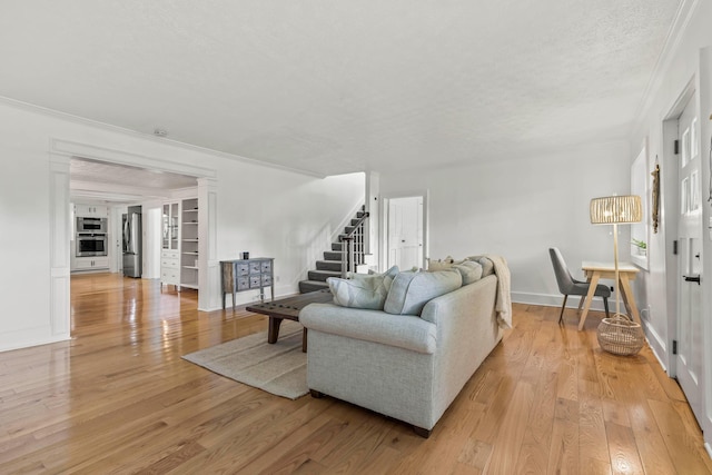 living room with built in shelves, a textured ceiling, light hardwood / wood-style flooring, and crown molding