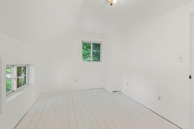 empty room featuring plenty of natural light, vaulted ceiling, and light hardwood / wood-style flooring