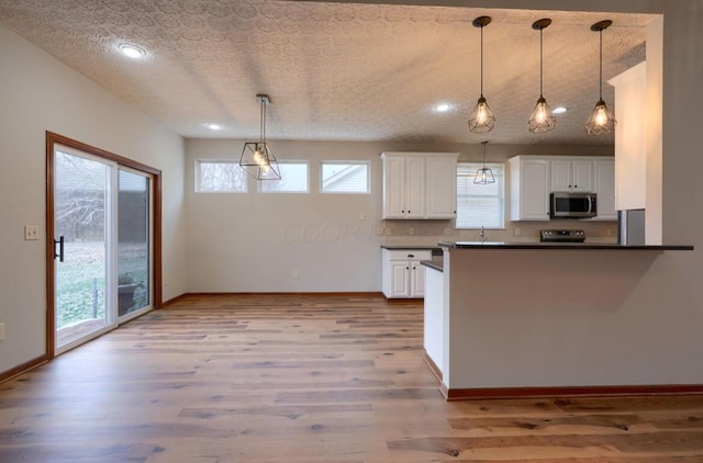 7265 Bromfield Dr, Canal Winchester, OH 43110 - kitchen featuring stainless steel microwave, dark countertops, white cabinets, a textured ceiling, and wood finished floors