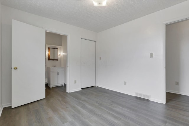 unfurnished bedroom featuring connected bathroom, a closet, a textured ceiling, and hardwood / wood-style flooring