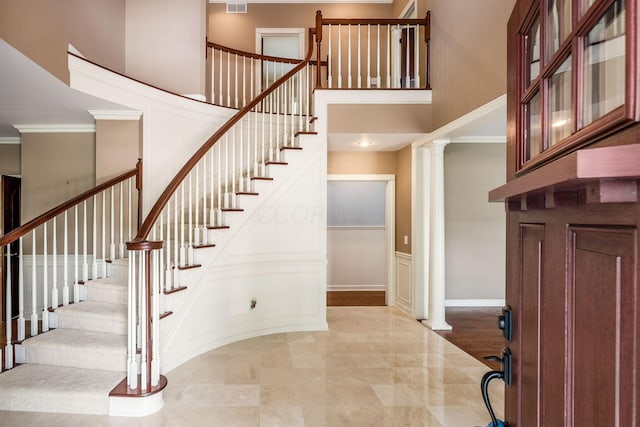 foyer entrance with ornate columns, a towering ceiling, light wood-type flooring, and ornamental molding