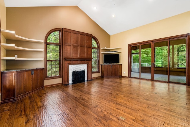 unfurnished living room with a fireplace, wood-type flooring, high vaulted ceiling, and plenty of natural light