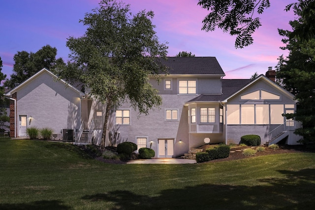 back house at dusk with a lawn, central AC, and french doors