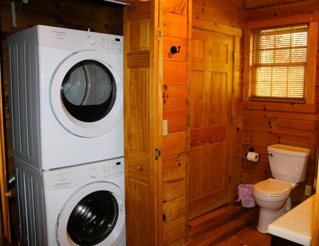 clothes washing area with dark hardwood / wood-style flooring, wood walls, and stacked washing maching and dryer