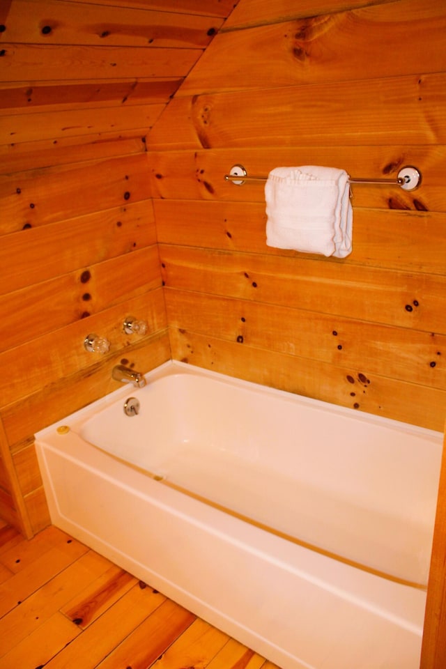 bathroom featuring wood-type flooring, wooden walls, and a tub