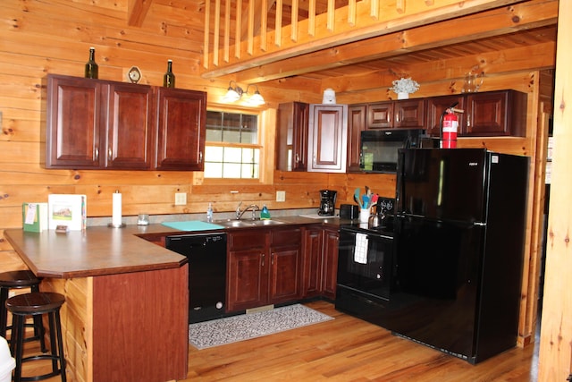 kitchen featuring wooden walls, black appliances, sink, a breakfast bar area, and kitchen peninsula