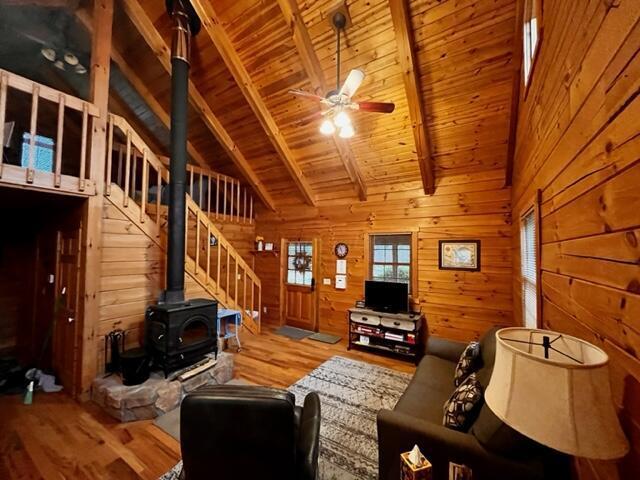 living room featuring beamed ceiling, wood walls, light hardwood / wood-style floors, and a wood stove