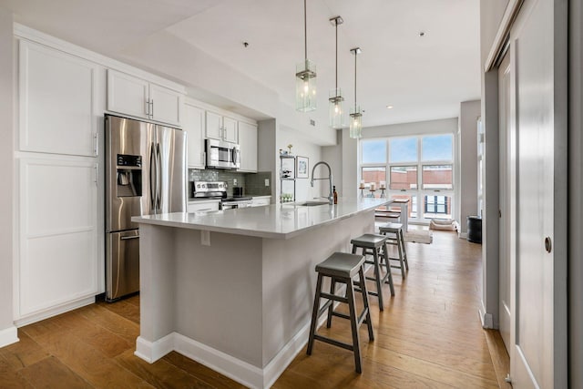 kitchen featuring white cabinets, a spacious island, light wood-type flooring, decorative light fixtures, and stainless steel appliances