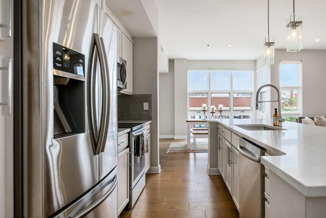 kitchen with sink, dark hardwood / wood-style floors, pendant lighting, a kitchen island with sink, and appliances with stainless steel finishes