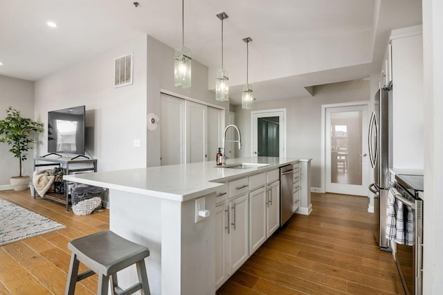 kitchen featuring light wood-type flooring, stainless steel appliances, a kitchen island with sink, sink, and white cabinets