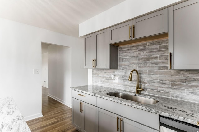 kitchen with decorative backsplash, light stone countertops, stainless steel dishwasher, sink, and dark hardwood / wood-style floors