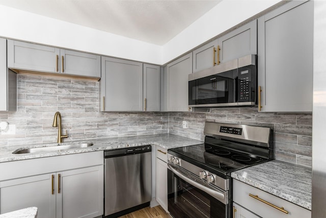 kitchen featuring gray cabinetry, sink, stainless steel appliances, light stone counters, and backsplash