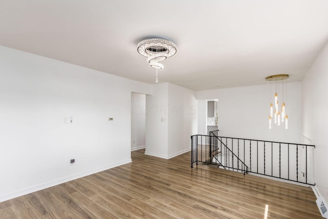 spare room with hardwood / wood-style floors and a notable chandelier