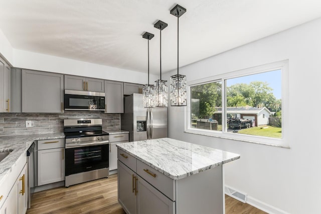 kitchen with decorative backsplash, appliances with stainless steel finishes, decorative light fixtures, dark hardwood / wood-style floors, and a kitchen island