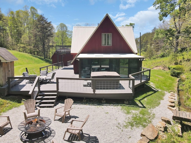 rear view of property featuring a lawn, a sunroom, a fire pit, and a deck