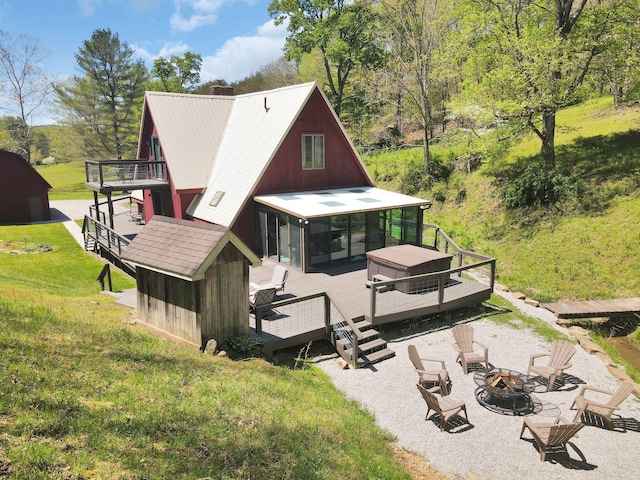 rear view of house with a fire pit, a sunroom, a deck, and a lawn