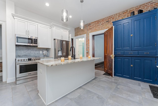 kitchen with decorative light fixtures, brick wall, an island with sink, and appliances with stainless steel finishes