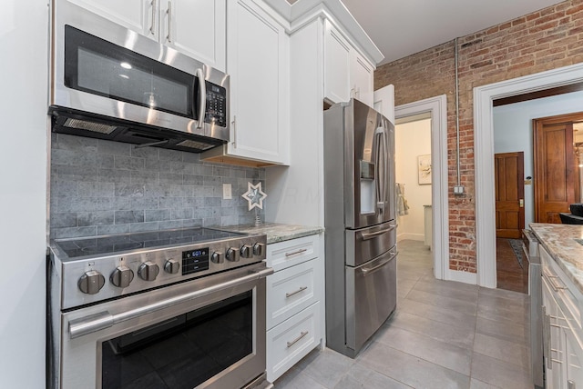 kitchen featuring light stone countertops, white cabinets, stainless steel appliances, and brick wall