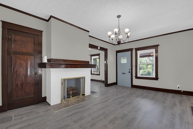 interior space featuring crown molding, a brick fireplace, a textured ceiling, light hardwood / wood-style floors, and a chandelier